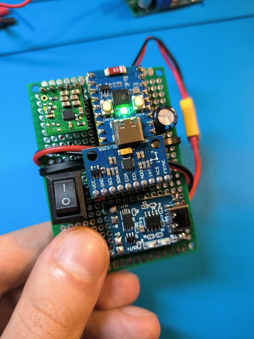 ESP32-C3 + MPU-6050 IMU sensor node on perfboard, hand-soldered, green power LED active, held in hand against blue silicone mat