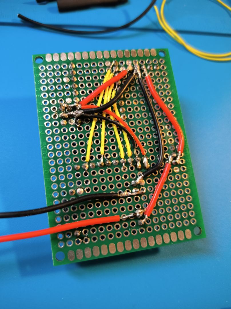 Perfboard bottom side showing hand-soldered wire routing — red, yellow, and black wires connecting power and signal traces