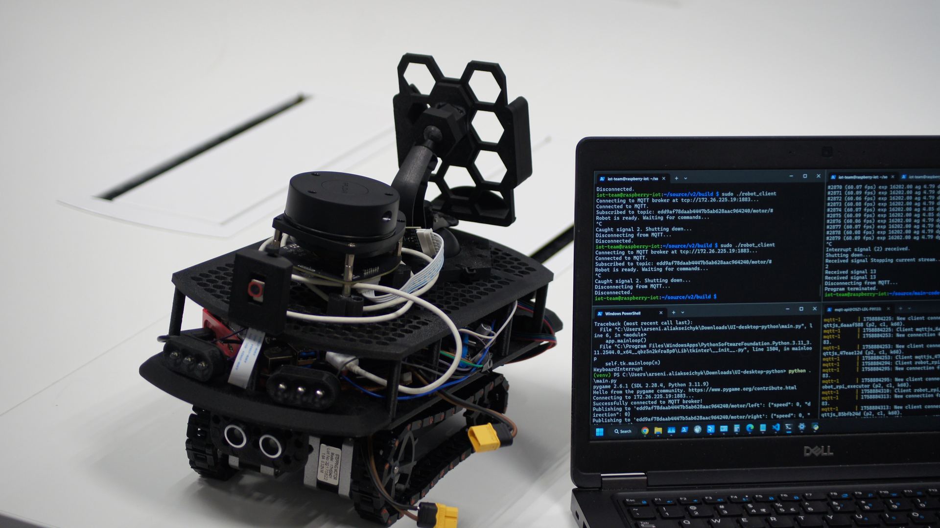 Tracked robot next to Dell laptop running live MQTT telemetry: robot_client connected, subscribed to motor topics, 'Robot is ready' status visible in terminal